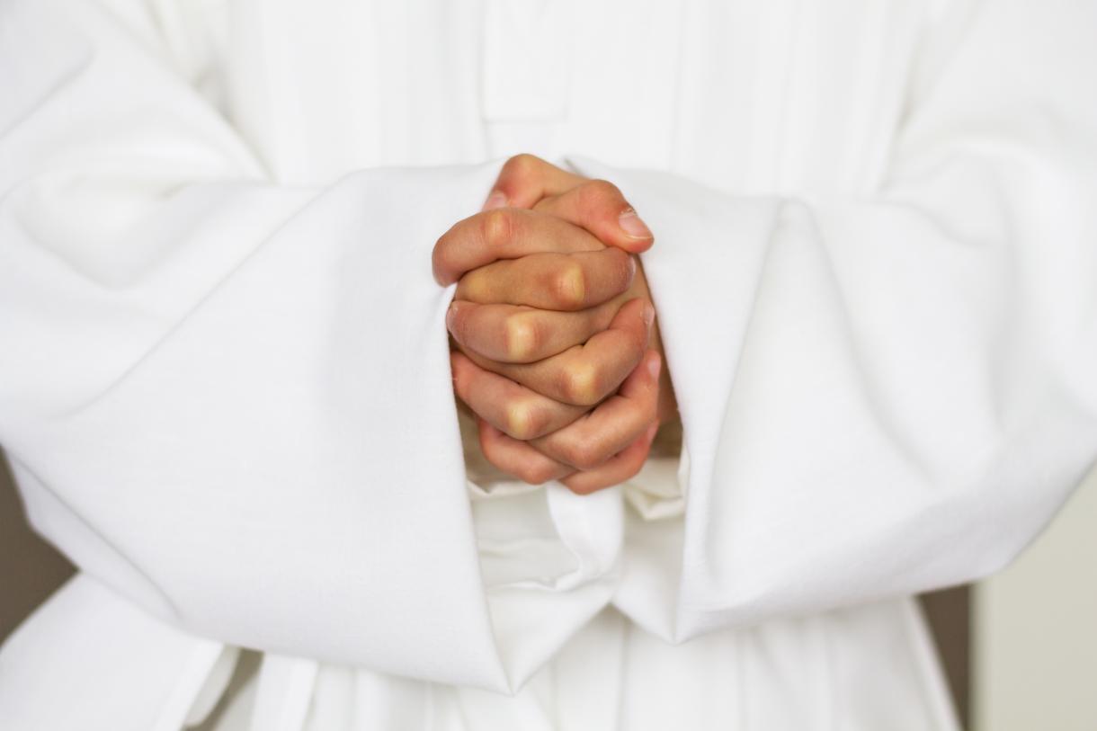 clergyperson in white robe clasps their hands